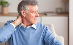 A man in his sixties massaging his neck to relieve arthritis pain. Schedule an appointment for an arthritis symptoms and treatment checkup.